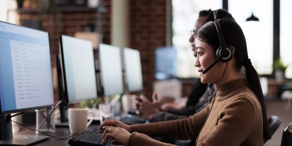Paralyzed asian employee working at call center reception in disability friendly office. Female operator wheelchair user with impairment giving assistance on customer service helpline.